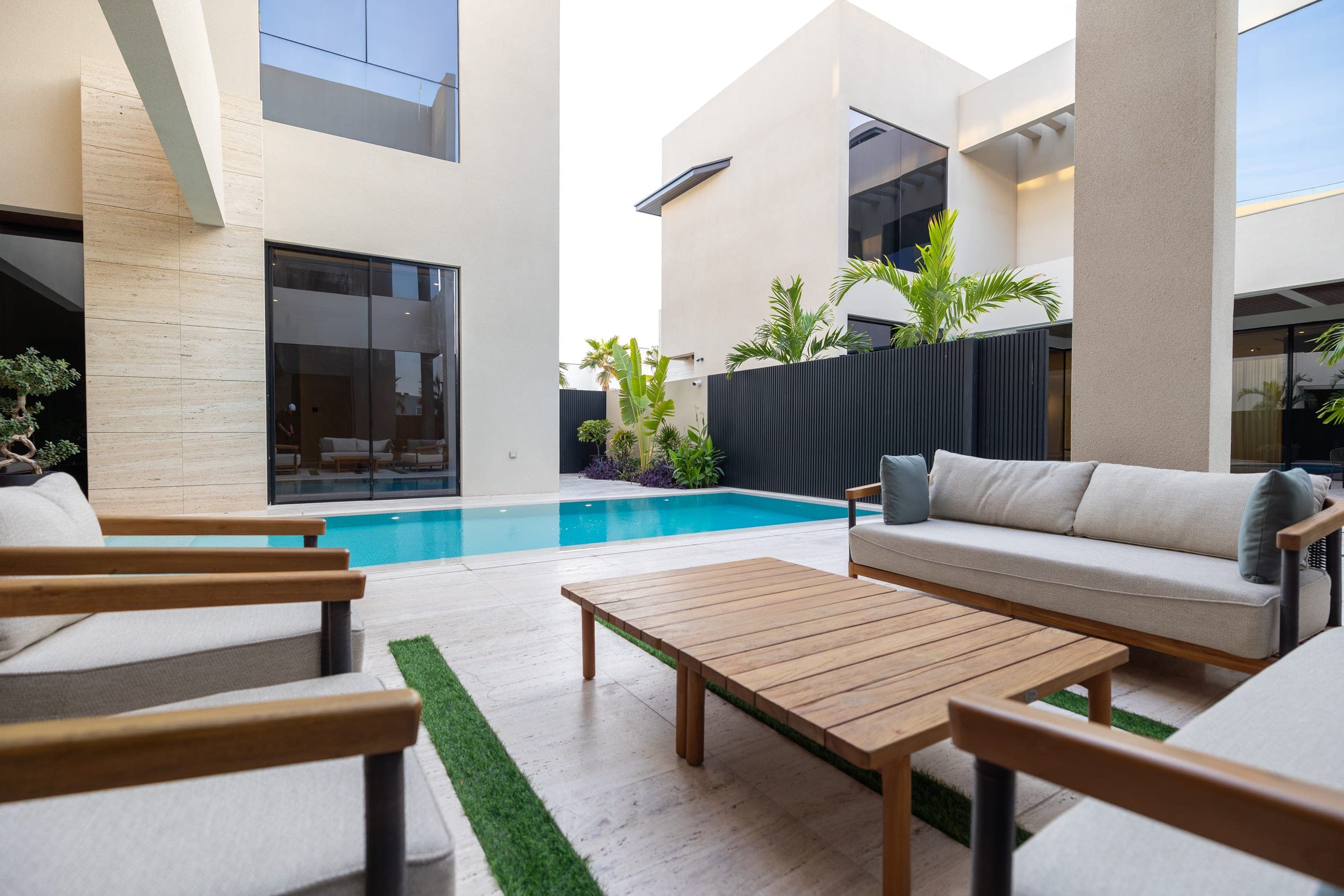 Private pool courtyard by LKYOOB — cream lounge sofas and a teak table beside a still pool, framed by pale stone villa walls